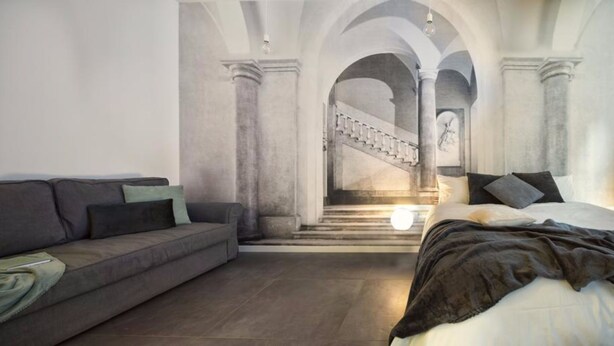 A modern living room with a sofa, a bed, and a staircase leading to an upper level. - Suite Vogue Sforza (Voghera)