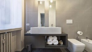 A modern bathroom with a large mirror, a sink, a toilet, and a shower area. - Suite Vogue Sforza (Voghera)