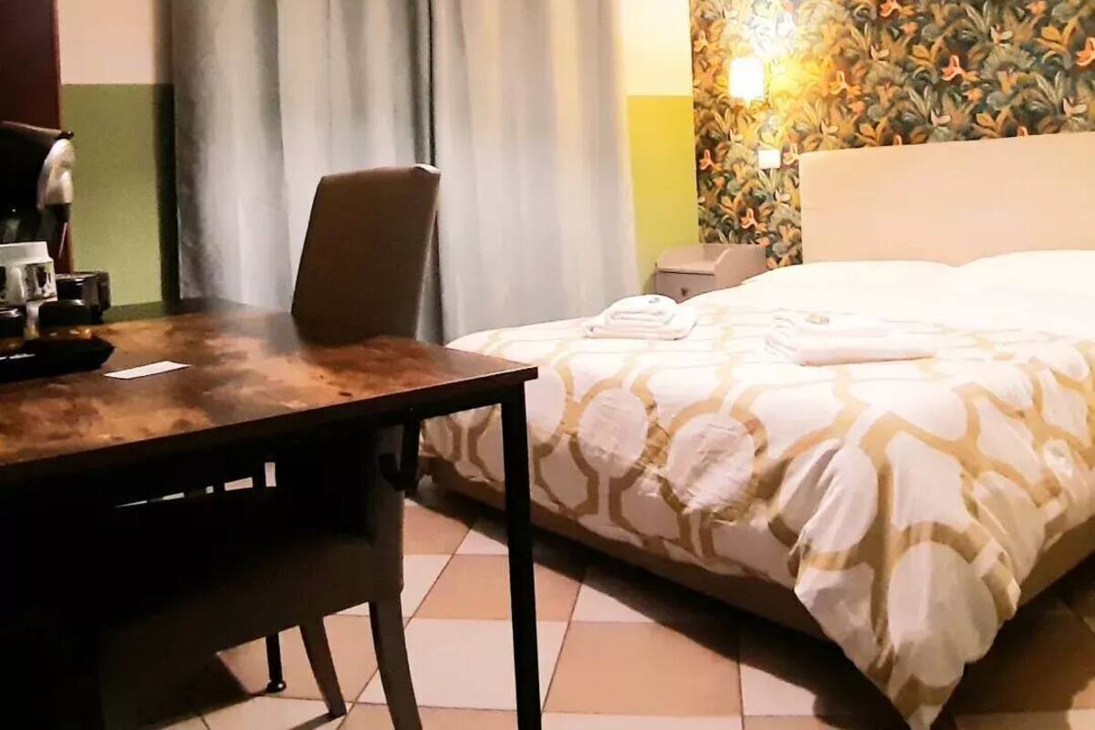 Une chambre d’hôtel avec un lit, un bureau et une chaise, une lampe et un mur décoré d’un motif.