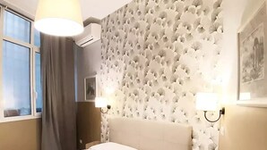 Habitación de hotel con cama, cabecera, dos lámparas fijadas a la pared, ventana con cortinas y pared con diseño.