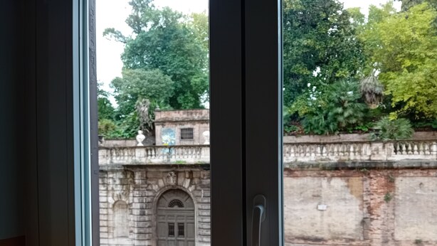 Vista a través de una ventana que muestra un edificio con pared de piedra y un gran arco.