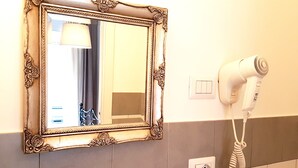 Un baño con espejo, secador de pelo, toallero y repisa de vidrio.