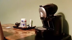 Una cafetera sobre una mesa con una taza y un plato, una bandeja y un pequeño recipiente.