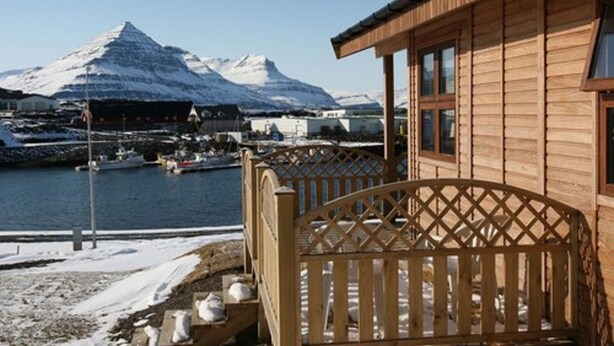 A wooden building with a balcony overlooking a harbor, with mountains in the background.