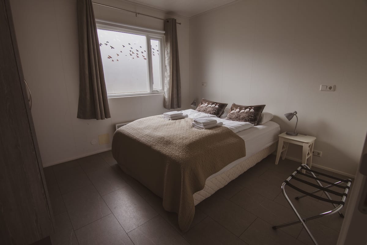 Ein Schlafzimmer mit Bett, einem Fenster mit Vorhängen, einem Nachttisch mit Lampe und einer Heizung.