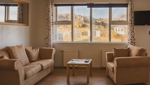 A living room with two beige sofas, a wooden coffee table, and a view of a rural landscape through large windows.