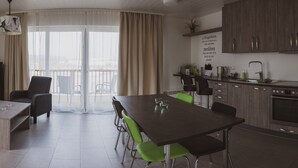 A modern living room with a sofa, a coffee table, and a dining area with chairs. There is a kitchen with cabinets and a sink.