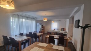 Comedor con mesas y sillas de madera, área de cocina con lavaplatos y estufa, y sala de estar con sofá y televisor.