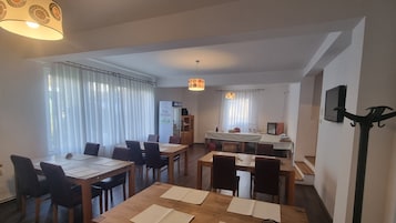 Comedor con mesas y sillas de madera, área de cocina con lavaplatos y estufa, y sala de estar con sofá y televisor.
