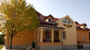 Un edificio con un letrero que dice "VILA PARC" y un área de estar al aire libre cubierta, con mesas y sillas.