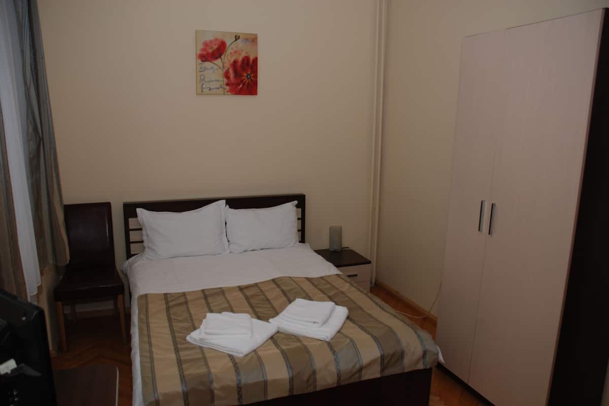 Un lit bien fait, avec du linge de lit blanc et une couvre-lit à rayures, une table de chevet avec une lampe, une chaise et une armoire.