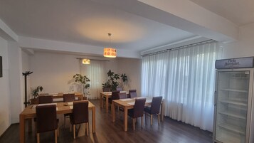 A dining area with wooden tables and chairs, a refrigerator, and a plant.