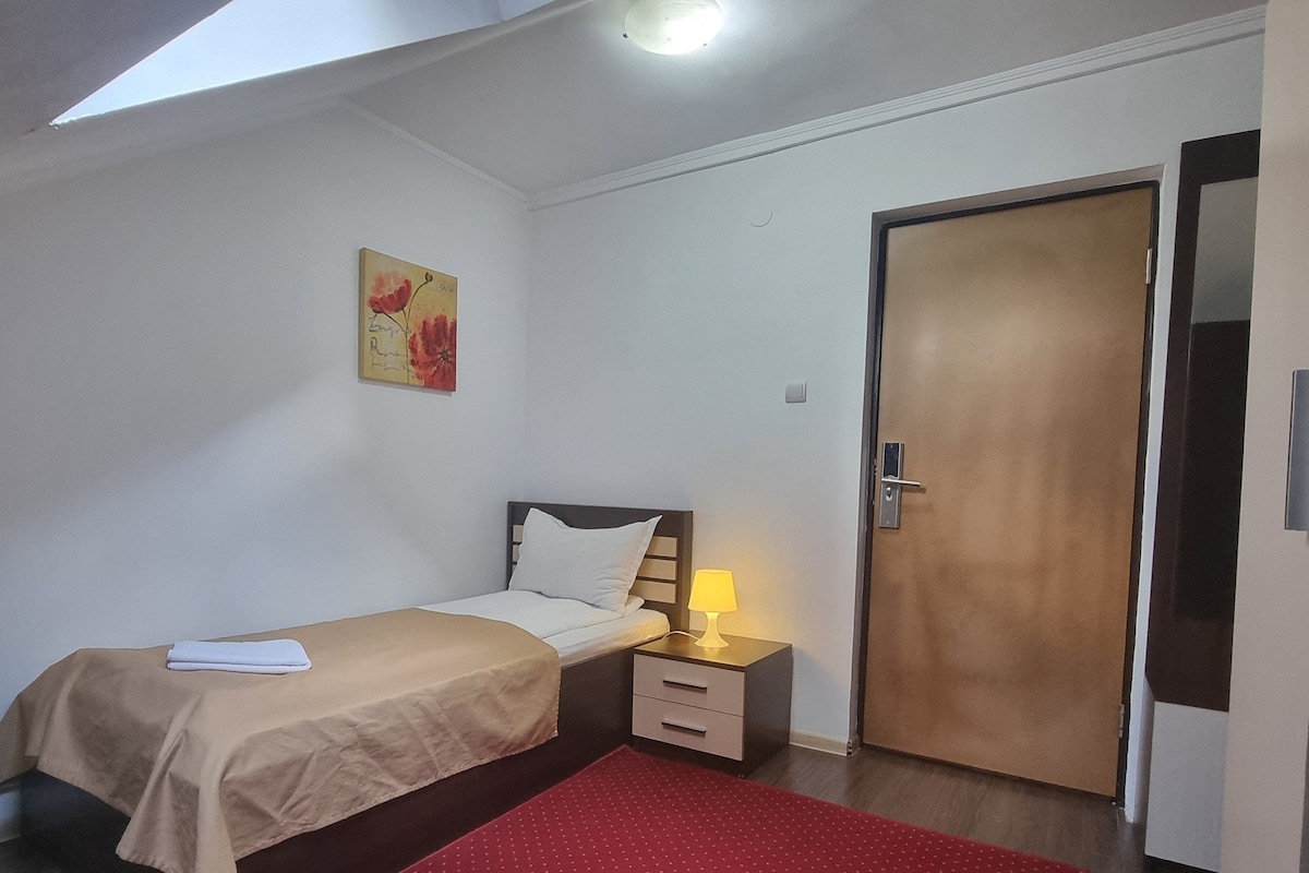 A bedroom with a bed, bedside table, lamp, and a door.