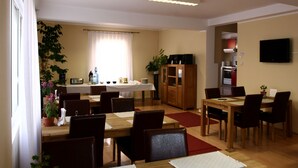 Un comedor con mesa y sillas de madera, una cocina con estufa y armarios, y un televisor montado en la pared.