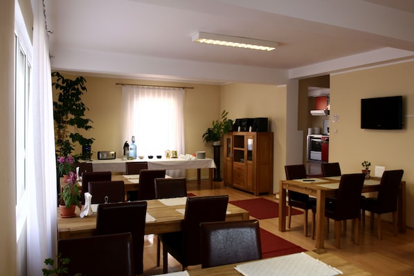 A dining area with a wooden table and chairs, a kitchen area with a stove and cabinets, and a television mounted on the wall.