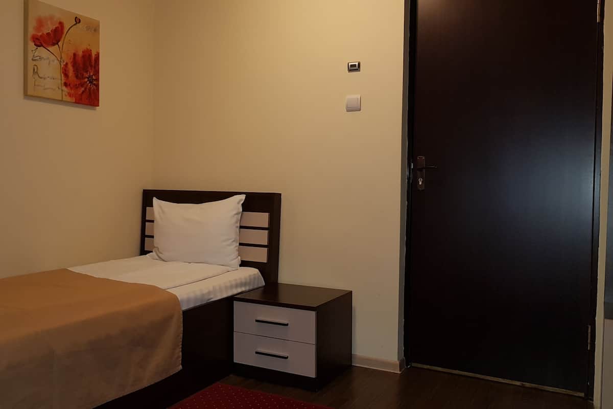 Une chambre à coucher avec un lit, une table de chevet, un tiroir, une porte et un tableau au mur.