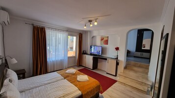 A hotel room with a bed, a desk with a television, a red rug, and a view of the outside.