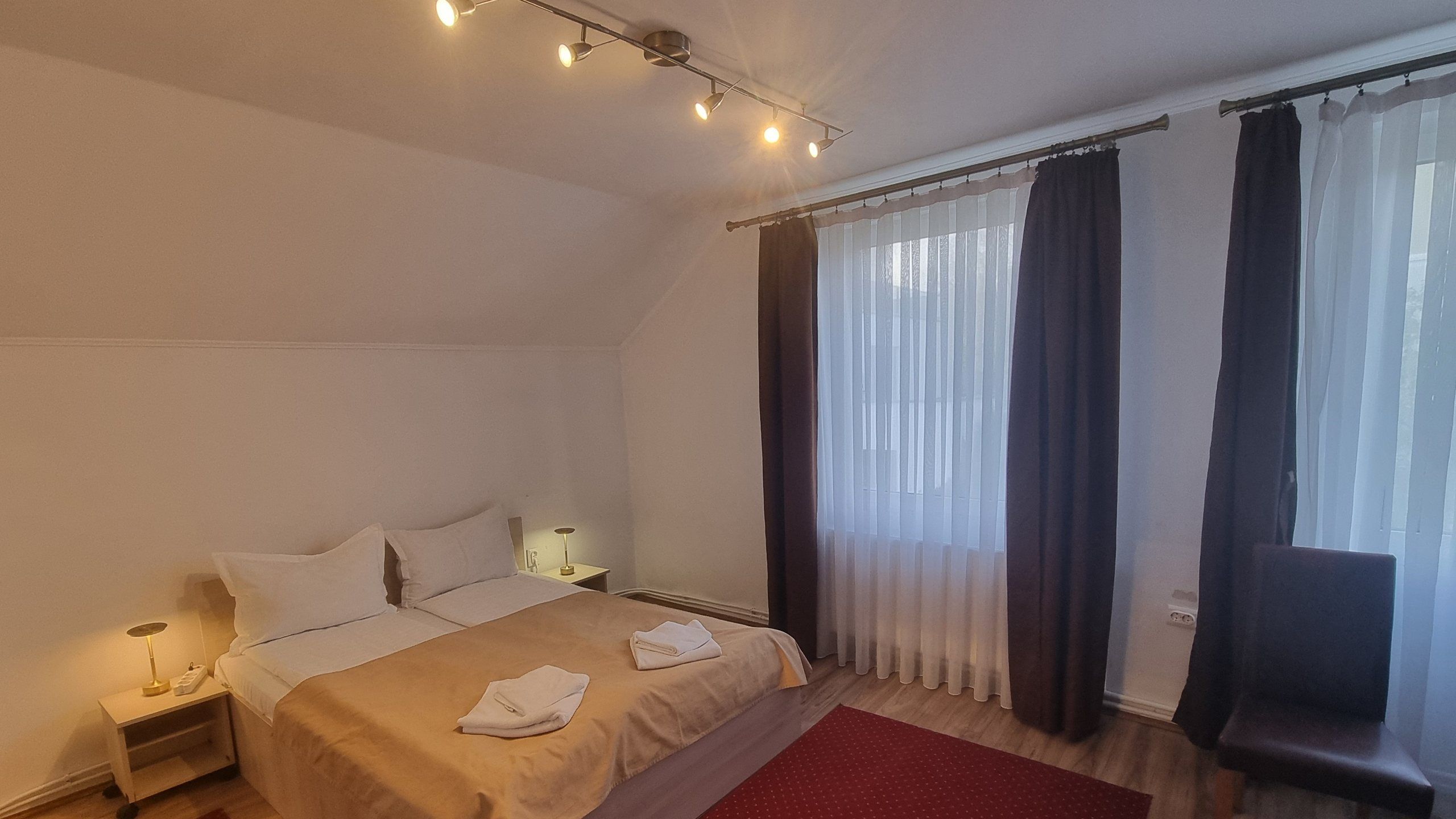 Una habitación de hotel con cama, mesitas de noche, lámpara, cortinas y ventana.
