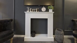 A modern living room with a white fireplace, a flat-screen TV mounted above it, and two dark sofas. - Suite Vogue Visconti (Voghera)