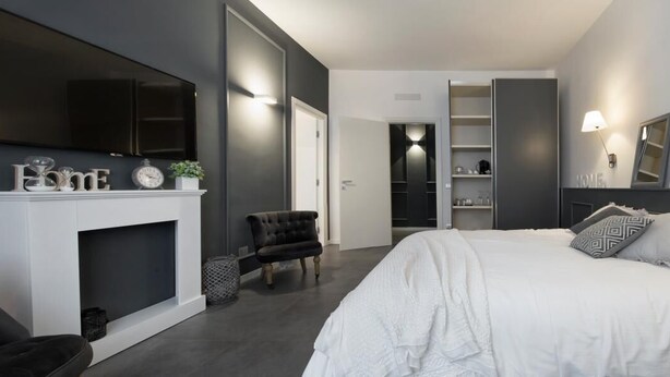 A modern bedroom with a large bed, a TV mounted on the wall, and a fireplace. - Suite Vogue Visconti (Voghera)