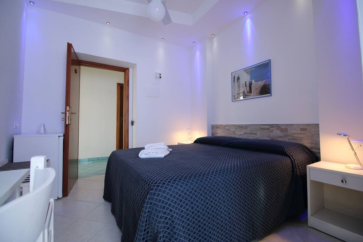A bedroom with a bed, bedside table, and a door leading to another room.