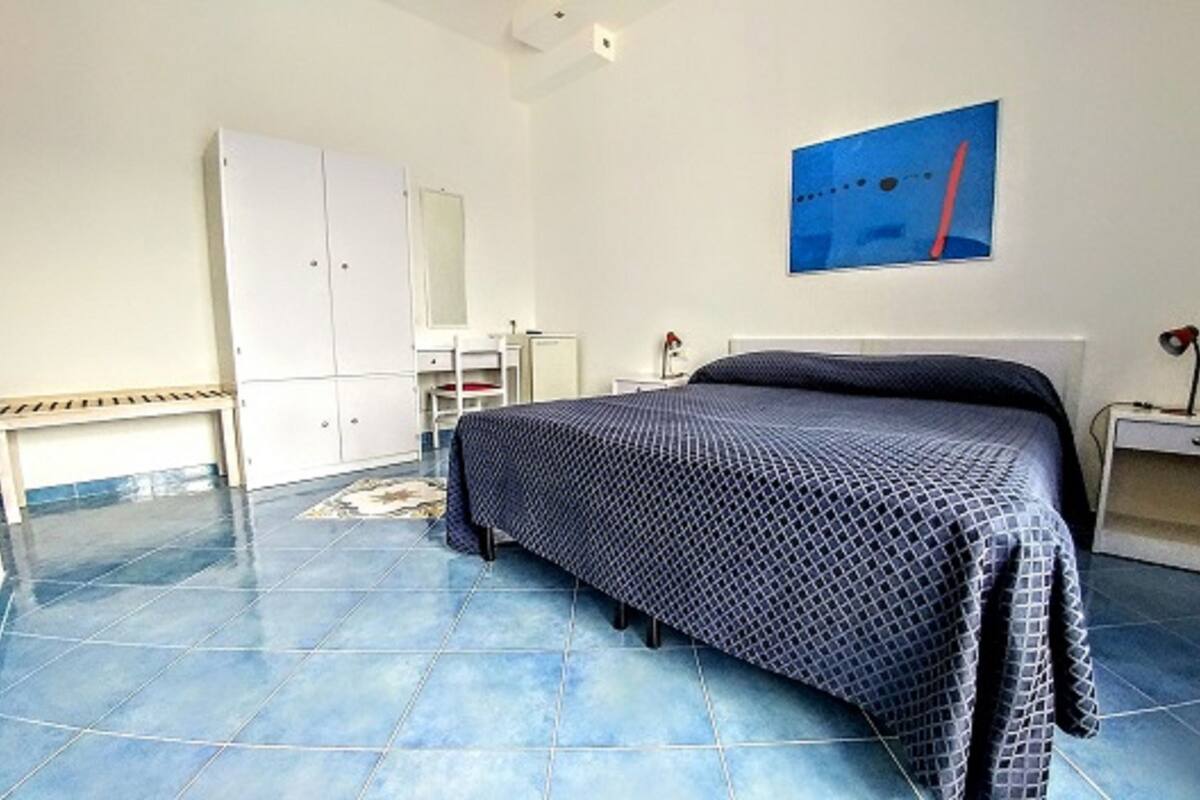 A bedroom with a bed, a nightstand, a desk, a wardrobe, and a painting on the wall.