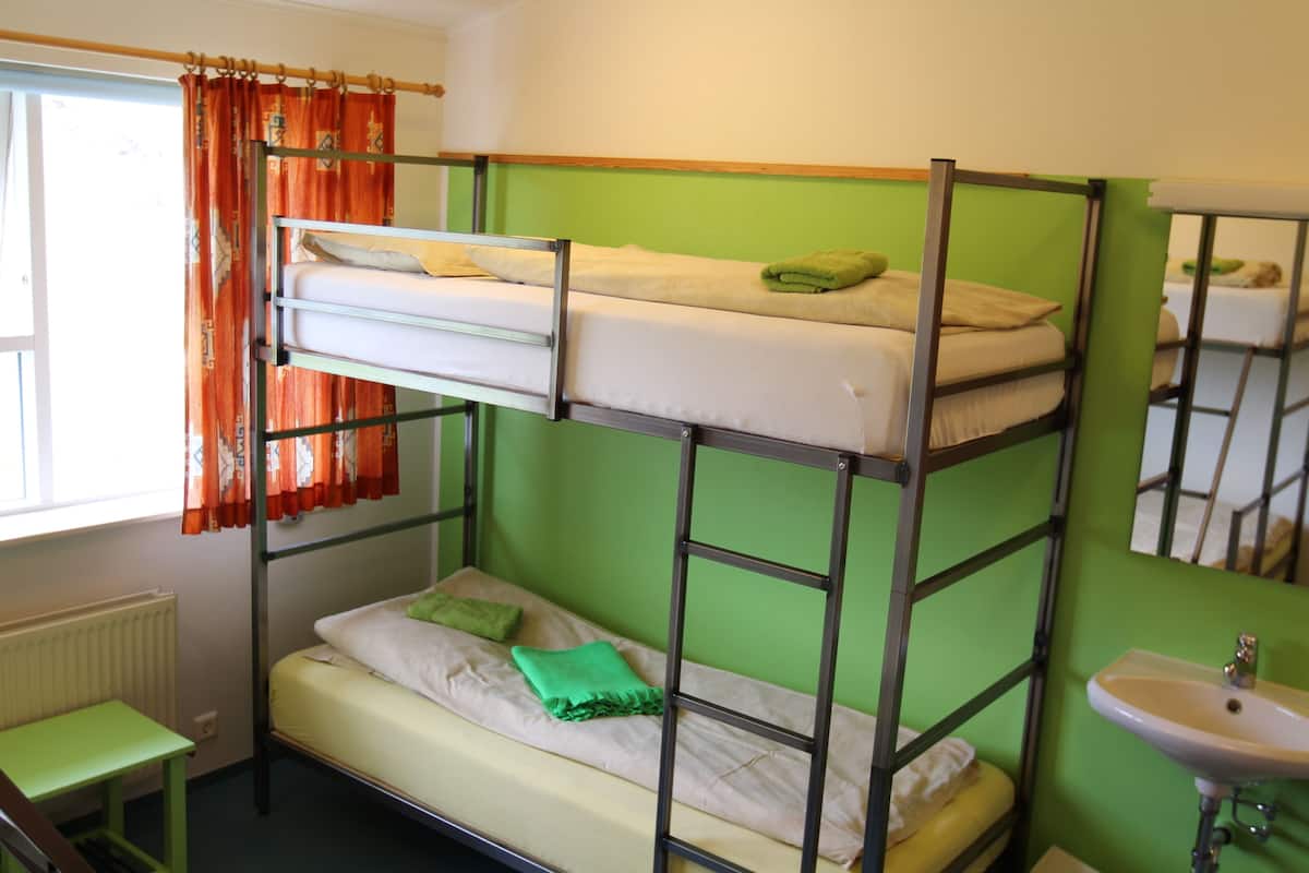Ein Schlafraum mit Etagenbetten, einer grünen Wand, einem Fenster mit orangefarbenen Vorhängen, einem kleinen Tisch und einem Waschbecken.