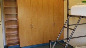 A room with a wooden wardrobe, a metal bunk bed, and a shelving unit. - Helgafell Hostel (Djupivogur)