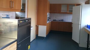 A compact kitchen with wooden cabinets, a built-in oven, a refrigerator, and a microwave. - Helgafell Hostel (Djupivogur)