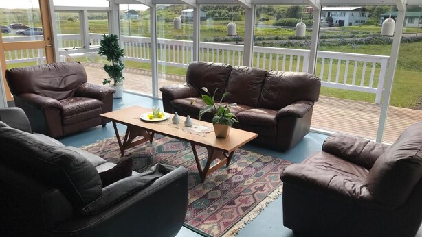 A conservatory with a view of a green landscape, furnished with leather sofas and a coffee table. - Helgafell Hostel (Djupivogur)
