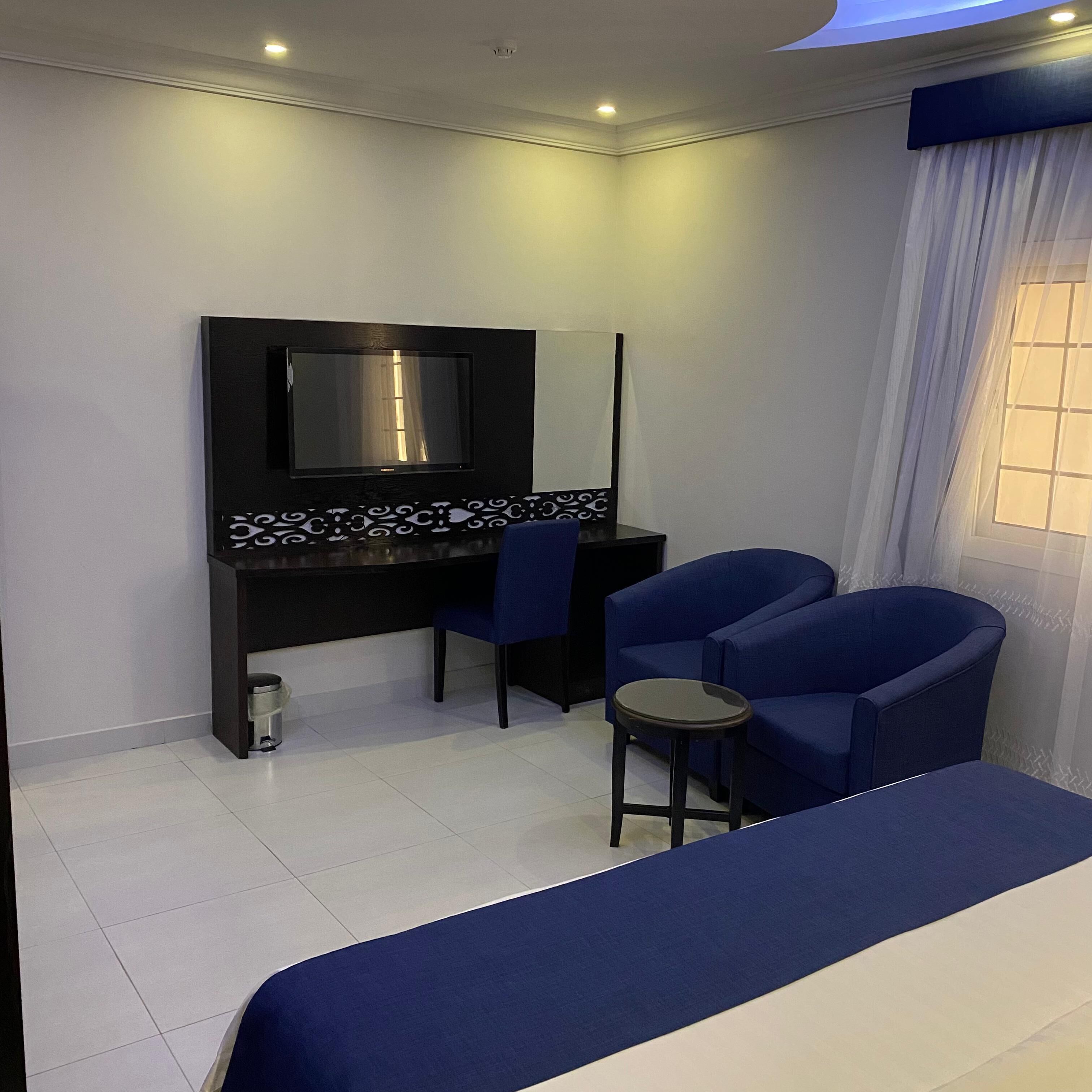 A hotel room with a bed, a desk with a chair, a TV, and a window with curtains.