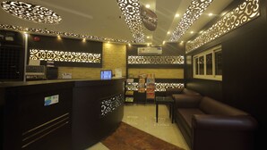 Un espace d’accueil doté d’un comptoir de réception sombre, d’un coin salon avec un canapé en cuir marron et de panneaux muraux décoratifs.