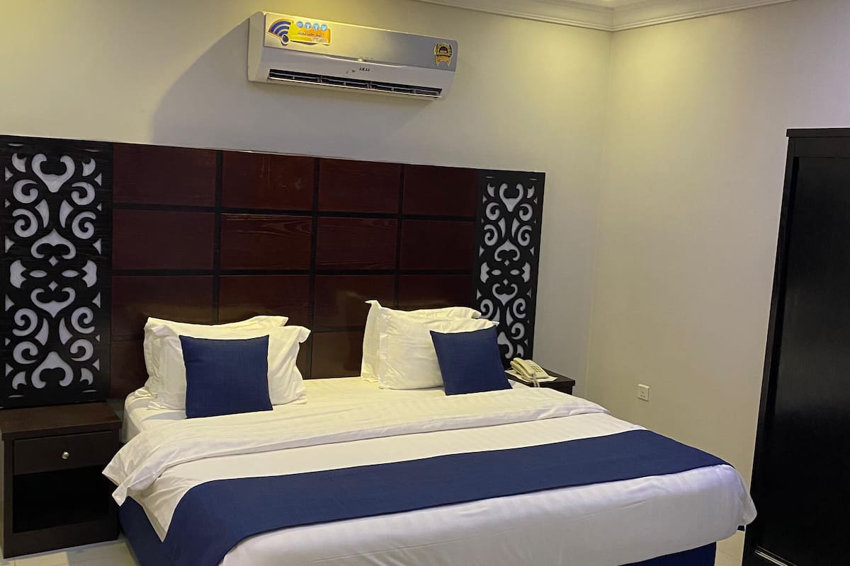 Une chambre d’hôtel moderne avec un grand lit, une table de chevet, une lampe de chevet, un téléphone et un climatiseur fixé au mur.