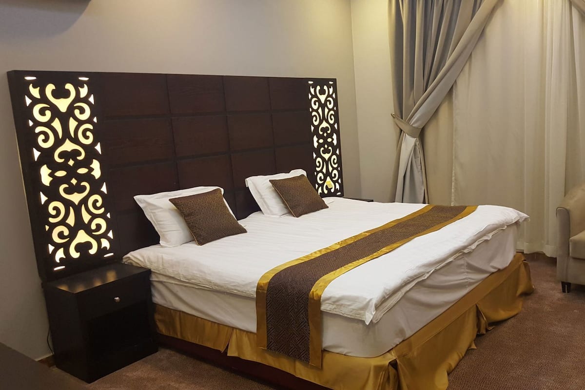 Une chambre d’hôtel avec un grand lit, deux oreillers, une table de chevet, une chaise et une tête de lit décorative.