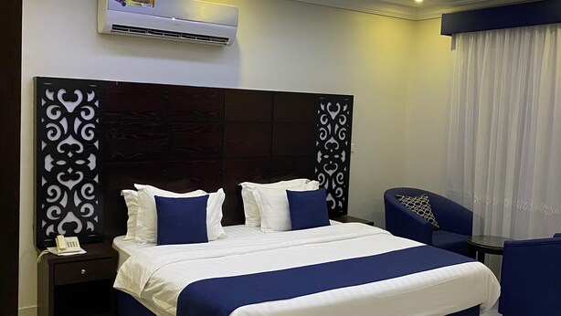 Une chambre d’hôtel moderne avec un grand lit, une table de chevet avec un téléphone, un bureau et une chaise. On y trouve également un luminaire au plafond et un appareil de climatisation.