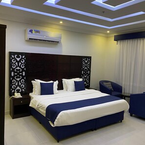 A modern hotel room with a large bed, a bedside table with a phone, a desk, and a chair. There is a ceiling light fixture and an air conditioning unit. - City Center Plaza Aparthotel (Jeddah)