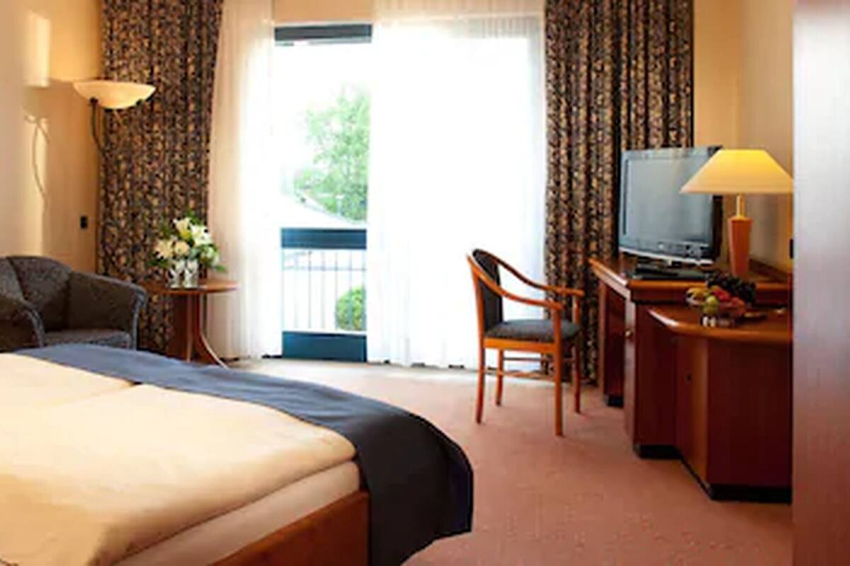 Una habitación de hotel con una cama, un escritorio con televisor, una silla y una mesita con flores.
