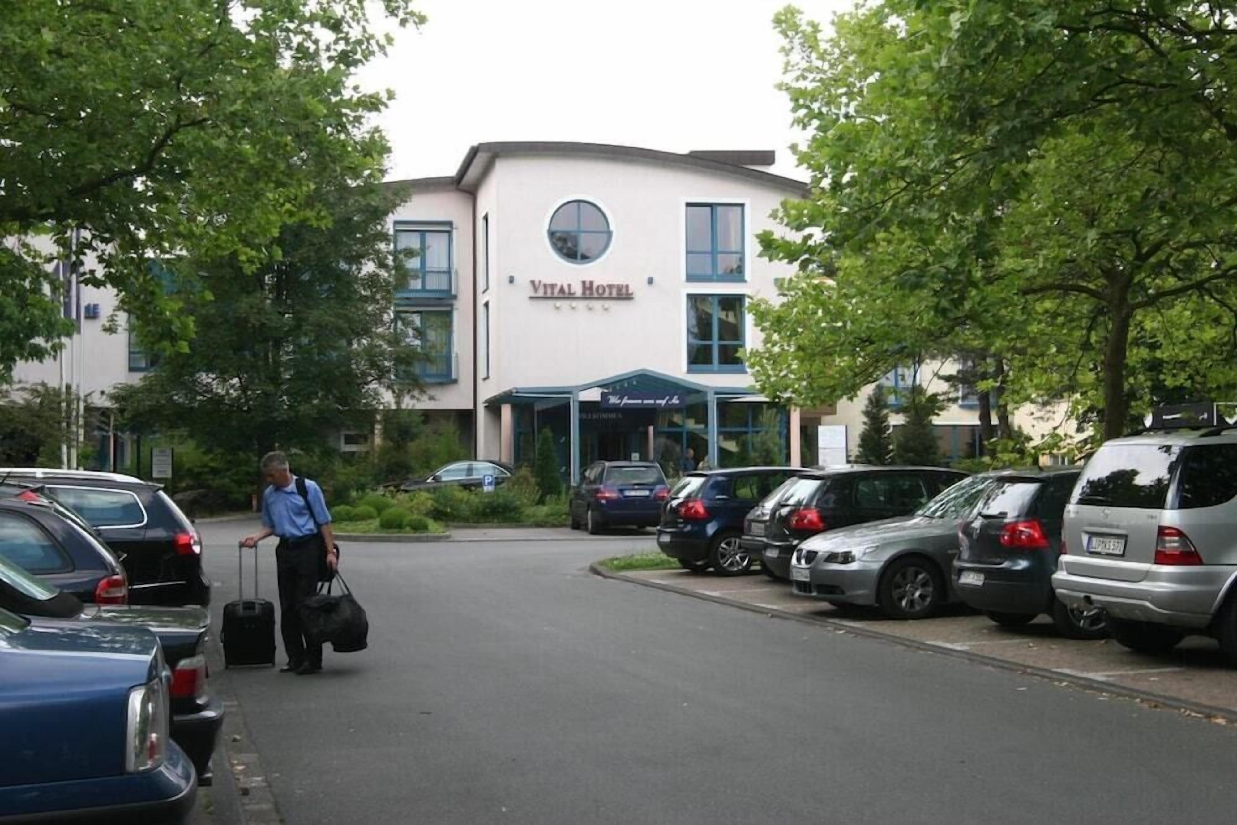 Un edificio con la leyenda 'Vital Hotel', un estacionamiento y varios coches aparcados.