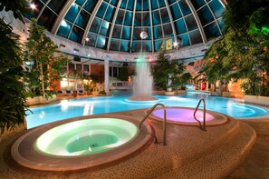 A large indoor swimming pool with multiple hot tubs, a waterfall feature, and a glass-domed ceiling. - Vital Hotel Westfalen Therme (Bad Lippspringe)