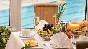 A breakfast table with a fruit bowl, croissants, and orange juice by a poolside window. - Vital Hotel Westfalen Therme (Bad Lippspringe)