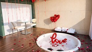 Una habitación con bañera, globos con forma de corazón y una mesa de vidrio con sillas.