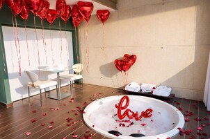 Una habitación con bañera, globos con forma de corazón y una mesa de vidrio con sillas.