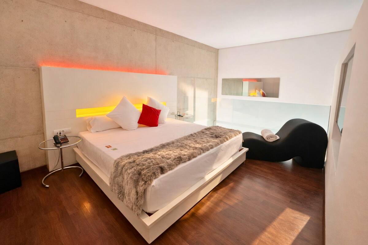 A modern bedroom with a large bed, bedside table, and a built-in bench with a towel.