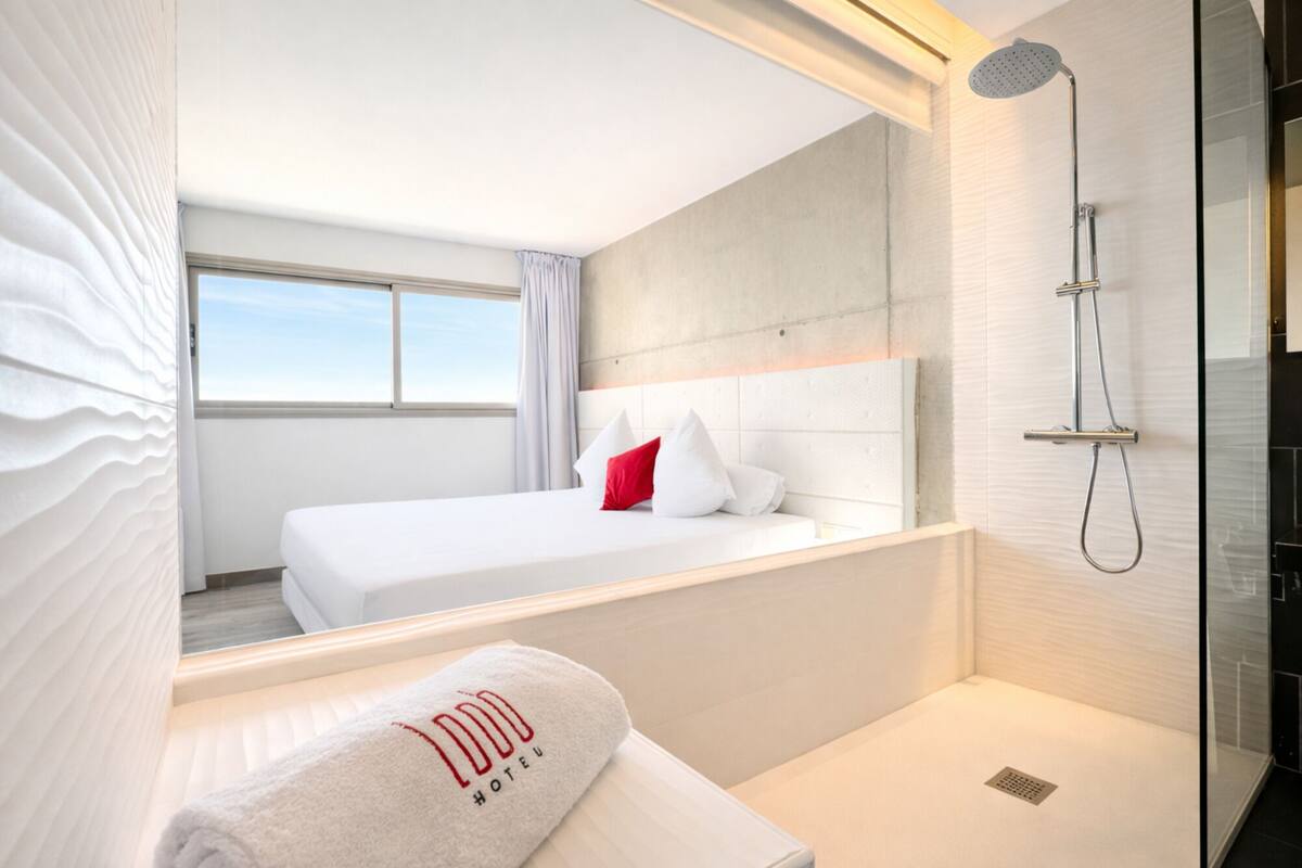 A hotel room with a bed, a shower, and a view of the sky.