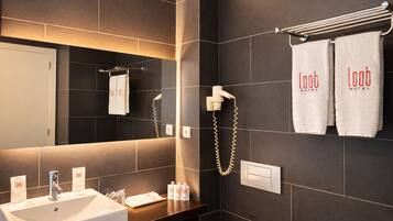 Un baño moderno con un espejo grande, un lavabo, un perchero con dos toallas y un secador de pelo.