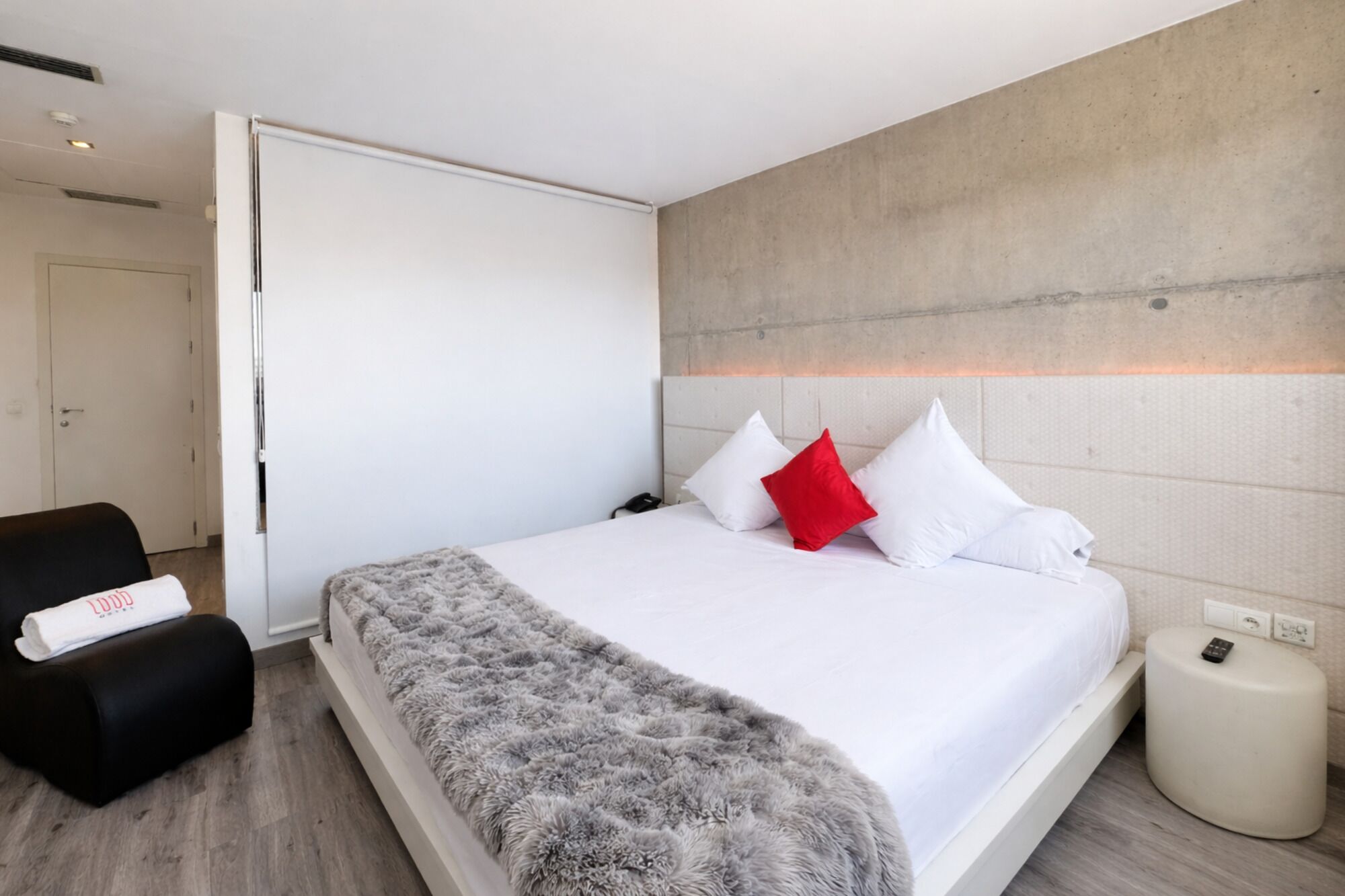 Una habitación de hotel moderna con una cama grande, una silla negra y una mesita de noche pequeña.