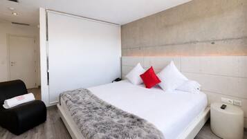 Una habitación de hotel moderna con una cama grande, una silla negra y una mesita de noche pequeña.