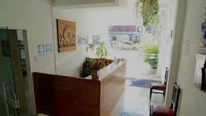 A reception desk with a wooden finish, a potted plant with red flowers, and a sign that reads "SUN DRIVER". - Hotel Sun River (Barranquilla)