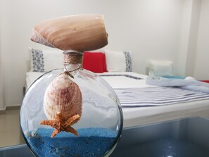 A clear glass terrarium with a starfish and a shell on top, placed on a table in a room with a bed and pillows in the background. - Hotel Sun River (Barranquilla)
