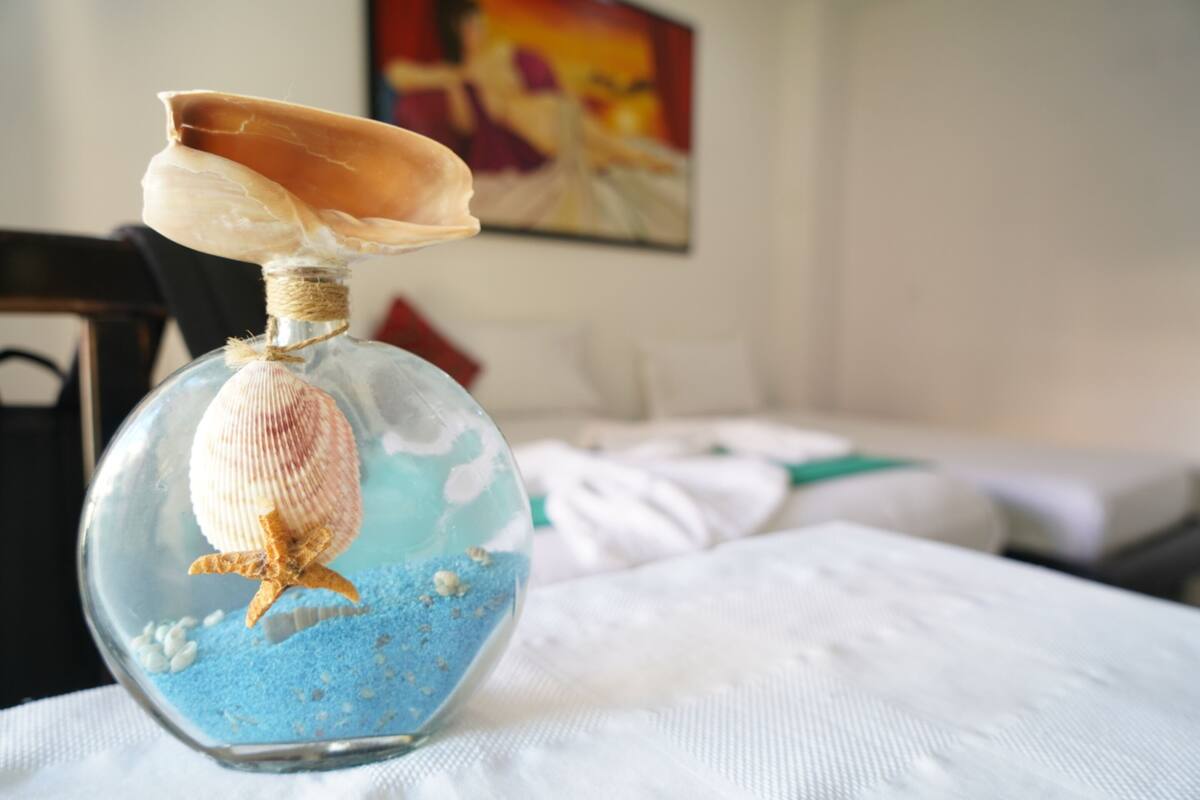 A clear glass bottle with a seashell and starfish inside, placed on a white surface with a painting in the background.
